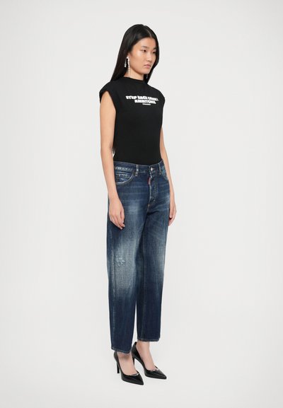 Camiseta negra ajustada con texto blanco, combinada con jeans rectos de tiro medio en azul oscuro desgastados y zapatos de tacón negros.