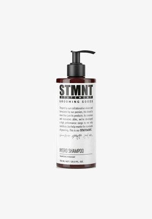 Bruine plastic fles met een zwarte pomp, gelabeld "HYDRO SHAMPOO" en "STMNT GROOMING GOODS." Textuur met een zwart-wit grafisch ontwerp.