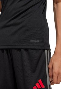 T-shirt de sport noir avec une texture lisse et une étiquette "AEROREADY" ; associé à un short noir avec des accents et des rayures rouges et grises.