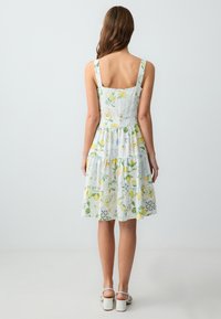 Bloem-geprinte zomerjurk met gele citroenen en groene accenten, voorzien van een gelaagde rok, vierkante halslijn en brede bandjes, gemaakt van lichtgewicht stof.