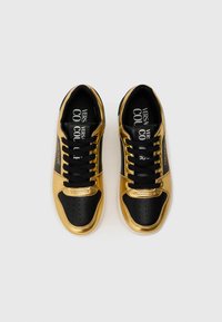 Sorte og gyldne sneakers med metallisk gylden syntetisk overdel, sort perforeret tå, flade sorte snørebånd og brandede sorte indersåler.