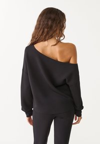 Sudadera negra con escote off-the-shoulder y mangas largas, hecha de tela suave. Estilo con un ajuste holgado. Combinada con pantalones negros a juego.