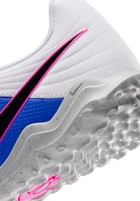 Bijela tenisica s plavim panelom, ružičasto-crnim Nike logotipom i teksturiranim sivim potplatom s uzorkom pjegica.