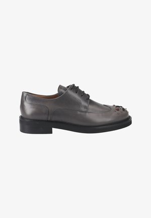 Gray leather lace-up shoe with rounded toe, featuring decorative metallic accents on the toe and a black rubber sole. Smooth texture.