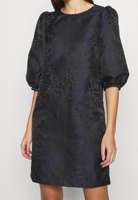Černé šaty s texturovaným fialovým zvířecím vzorem, krátké nabírané rukávy, kulatý výstřih a volný střih, sahající nad kolena.