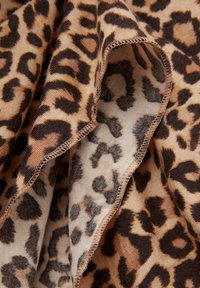 Leopardmønstret stof med en blanding af tan og brune farver, med en glat overflade og synlige sømme langs kanterne.