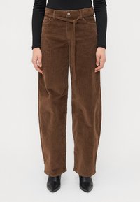 Pantaloni maro din catifea cord cu picioare largi, cu talie înaltă, detaliu cu brâu și textură în dungi, asortați cu pantofi negri cu vârf ascuțit.
