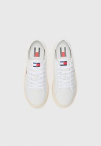 Vita sneakers med en slät läderövre, rund tå och snörningsdesign. Har en röd, vit och blå logotyp på tungan och sidan.