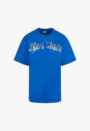 Kék pamut póló rövid ujjakkal, ezüst színű "Karl Kani" felirattal, vastag, stilizált betűtípussal a mellkason. Klasszikus kerek nyakú kialakítás.