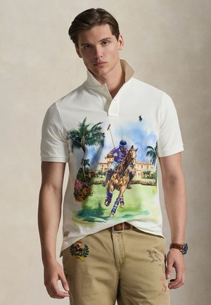Polo blanc arborant une illustration colorée d'un joueur de polo à cheval, avec des palmiers et une demeure en arrière-plan.