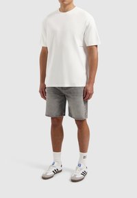 Witte katoenen T-shirt met korte mouwen, gecombineerd met grijze denim shorts. De schoenen hebben een kleurenschema van wit, grijs en blauw. Eenvoudig, casual ontwerp.