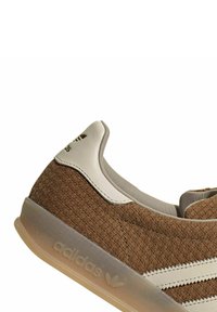 Sneaker intrecciato marrone con accenti beige, caratterizzato da una tomaia testurizzata, un tallone in pelle liscia e una suola in gomma traslucida con dettagli del logo.