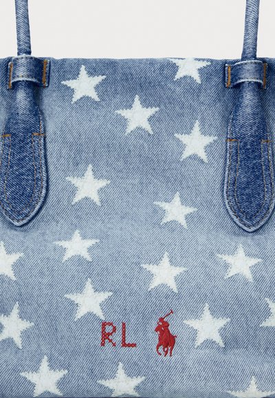 Denim rokassoma ar baltu zvaigžņu rakstu, kurai ir zilas rokas un sarkans izšūts logotips. Gluda tekstūra ar pastiprinātiem šuvju elementiem.