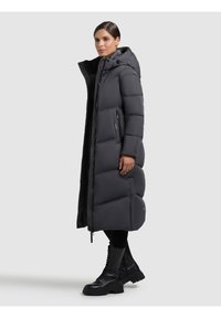 Dlouhá péřová bunda tmavě šedé barvy s kapucí, se zapínáním na zip a bočními kapsami, texturovaným prošívaným vzorem a štíhlým střihem.