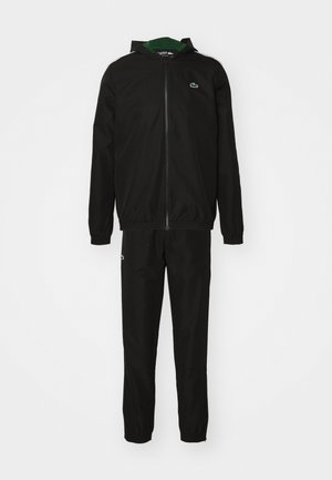 Chándal negro hecho de tela ligera. Presenta una chaqueta con capucha y cremallera y pantalones elásticos con un pequeño logo en el lado izquierdo del pecho y en el muslo.