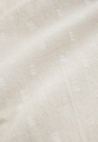 Soft cream-colored fabric with subtle raised dotted texture and fine weave in natural light.