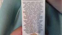 Svetlomodrý textilný štítok s pokynmi na starostlivosť a zložením materiálu: 80 % bavlna a 20 % polyester, so zahrnutými prekladmi do viacerých jazykov.