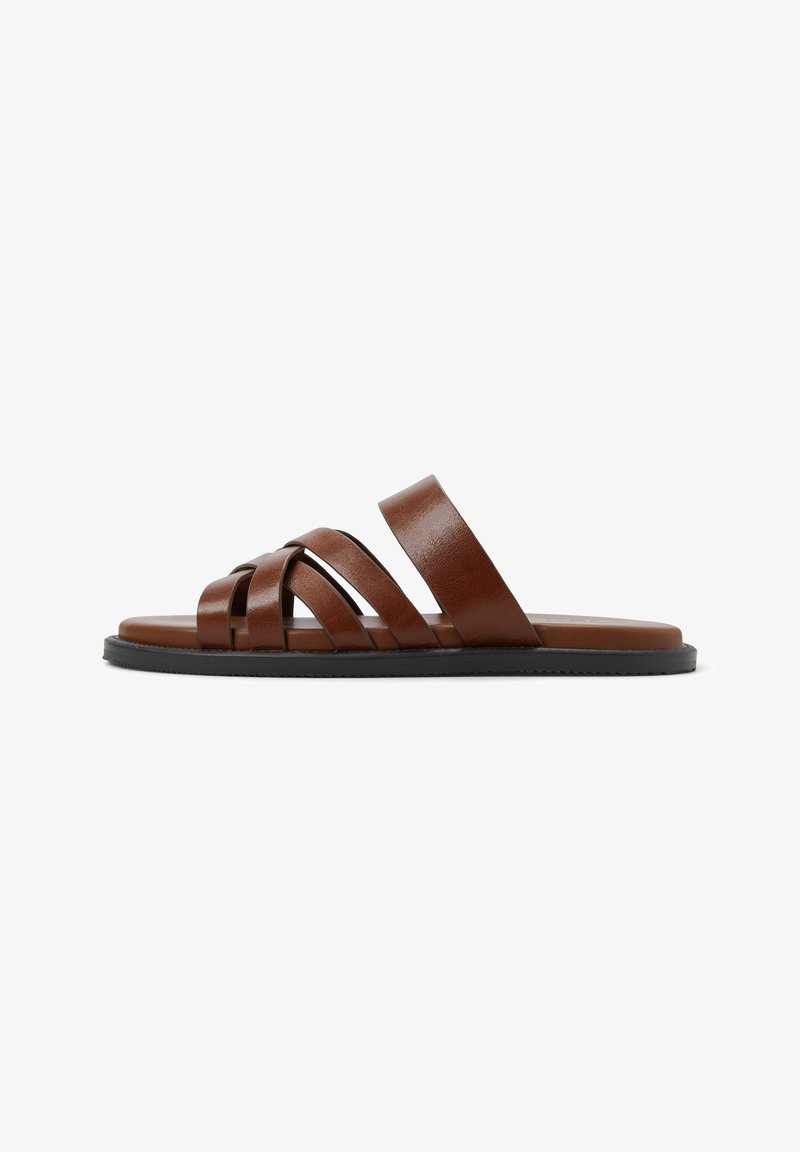 Brown leather slide sandals with overlapping straps, flat sole, and a smooth texture. Minimalist design with a rounded toe.