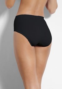 Mutande nere a vita alta in tessuto liscio con un bordo in pizzo a risvolto in vita, progettate per garantire comfort e copertura totale.