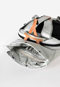 Silberner Rucksack mit schwarzen Akzenten, ausgestattet mit einem Reißverschluss, Innenfach und hellbraunen Lederträgern. Glattes Material und modernes Design.