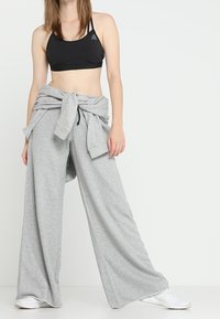 Svart sport-bh, ljusgrå vida sweatpants knutna i midjan, mjukt tyg, inga mönster, tillsammans med vita träningsskor.