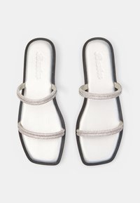 Sandalias planas blancas con punteras cuadradas, suelas negras y dos finas tiras brillantes sobre cada pie.