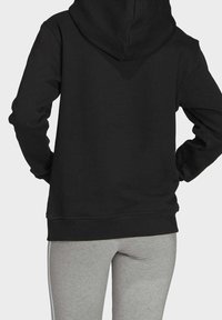 Svart huvtröja med en ficka fram och en justerbar huva, med ribbade ärmslut och nederkant, i kombination med grå sweatpants.