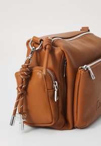 Borsa a tracolla in pelle marrone con doppia chiusura a zip, una tasca laterale e hardware in argento. Presenta un dettaglio in corda annodata sul tirazip.