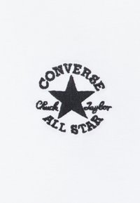 Černé vyšitěné logo s hvězdou a textem "Converse Chuck Taylor All Star" na bílém textilním pozadí.