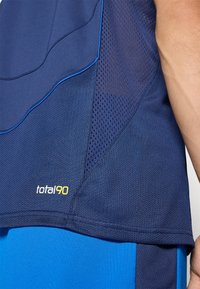 Cămașă sportivă de marină cu accente albastre și textură de plasă, prezentând cusături contrastante. Logo-ul "total90" este afișat în galben pe marginea inferioară.