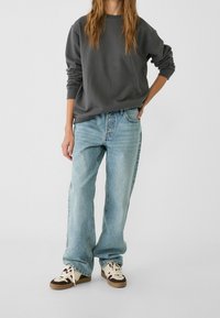 Sudadera gris de gran tamaño combinada con vaqueros holgados de color azul claro. Zapatillas con una mezcla de colores marrón oscuro y crema, con cordones prominentes.