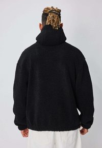 Veste en polaire noire surdimensionnée avec col montant et surface texturée. Caractérisée par des épaules tombantes et un ourlet élastiqué, offrant un ajustement confortable.