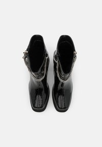 Černé kotníkové boty s lesklým povrchem imitující hadí kůži, které mají stříbrné řetízkové detaily a zipy na každé straně.