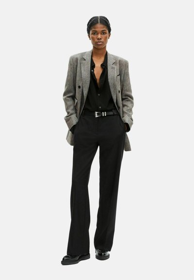 Blazer im grauen Hahnentritt-Muster, doppelt geknöpftes Design; schwarzes Hemd mit Knöpfen, schwarze Hosen und polierte schwarze Schuhe.