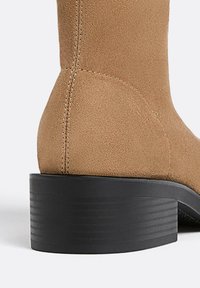 Stivale alla caviglia in suede marrone con punta rotonda e tacco a blocco nero texturizzato. Cuciture lungo il retro e superficie liscia.