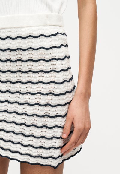 Λευκή πλεκτή φούστα με σκούρες μπλε κυματιστές ρίγες και υφή με ανάγλυφο σχέδιο. Το τελείωμα είναι κυματιστό και η μέση εφαρμοστή.