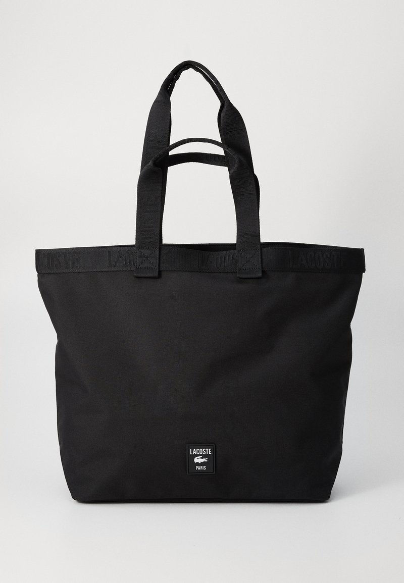 Borsa a tracolla nera Lacoste con doppi manici e dettaglio della tracolla con logo in rilievo, dotata di una piccola patta frontale con nome del marchio e icona del coccodrillo.