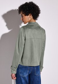 Grüne Wildlederjacke mit kragenförmigem Ausschnitt, hochgekrempelten Ärmeln und glatter Textur, kombiniert mit dunkelblauen Jeans.