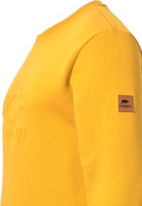 Sudadera de algodón amarilla con cuello redondo, detalle de logo texturizado en el pecho y una patch de cuero marrón en la manga etiquetada "Forsberg".