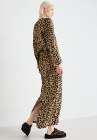 Løveprint maxi-kjole i tan og sort stoff, med lange ermer, belte i midjen, sidesplitt og parret med svarte slip-on sko.