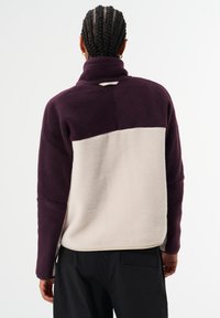 Fleece-Pullover in Lila und Creme mit hohem Kragen, strukturiertem Stoff und diagonalem Colorblock-Design. Einfacher flacher Saum.