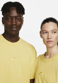 Tricouri din bumbac galben, cu guler rotund. Fiecare are un mic logo brodat Nike pe piept. Textură netedă, croială lejeră.