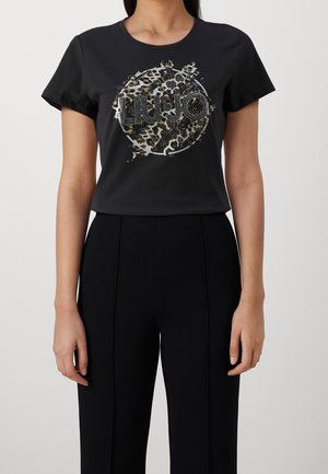Femme portant un T-shirt noir à manches courtes avec un imprimé léopard circulaire et le texte « LIU JO » orné de clous sur le devant.
