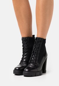 Bottines noires à lacets combinant cuir lisse et tissu texturé, talons épais, et design côtelé au niveau de la cheville.