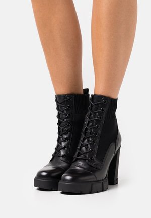 Stivaletti neri con lacci in pizzo che combinano pelle liscia e tessuto strutturato, tacchi robusti e design a coste alla caviglia.