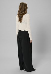 White textured long-sleeve top with a light blue accent and black wide-leg trousers. Simple design with relaxed fit, smooth fabric, and pockets.