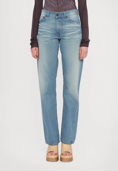 Hellblaue hochgeschnittene Jeans mit geraden Beinen, versehen mit einem verwaschenen Muster, fünf Taschen und einem Knopfverschluss. Kombiniert mit beigen Plateauschuhen.