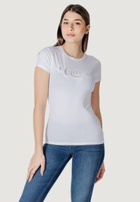 Witte, aansluitende t-shirt met korte mouwen, met een rhinestone "Guess" logo over de borst. Vlekkeloze katoenmateriaal, minimalistisch ontwerp.