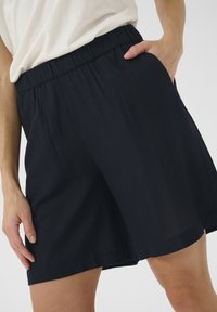Navy blue shorts made of lightweight fabric with an elastic waistband, side pockets, and a relaxed fit, featuring smooth, soft texture.