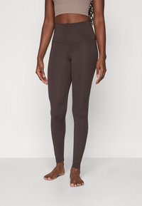 Højtaljede leggings i mørkebrun, lavet af strækbart stof. Har en glat tekstur og et enkelt design, der sidder tæt på kroppen.